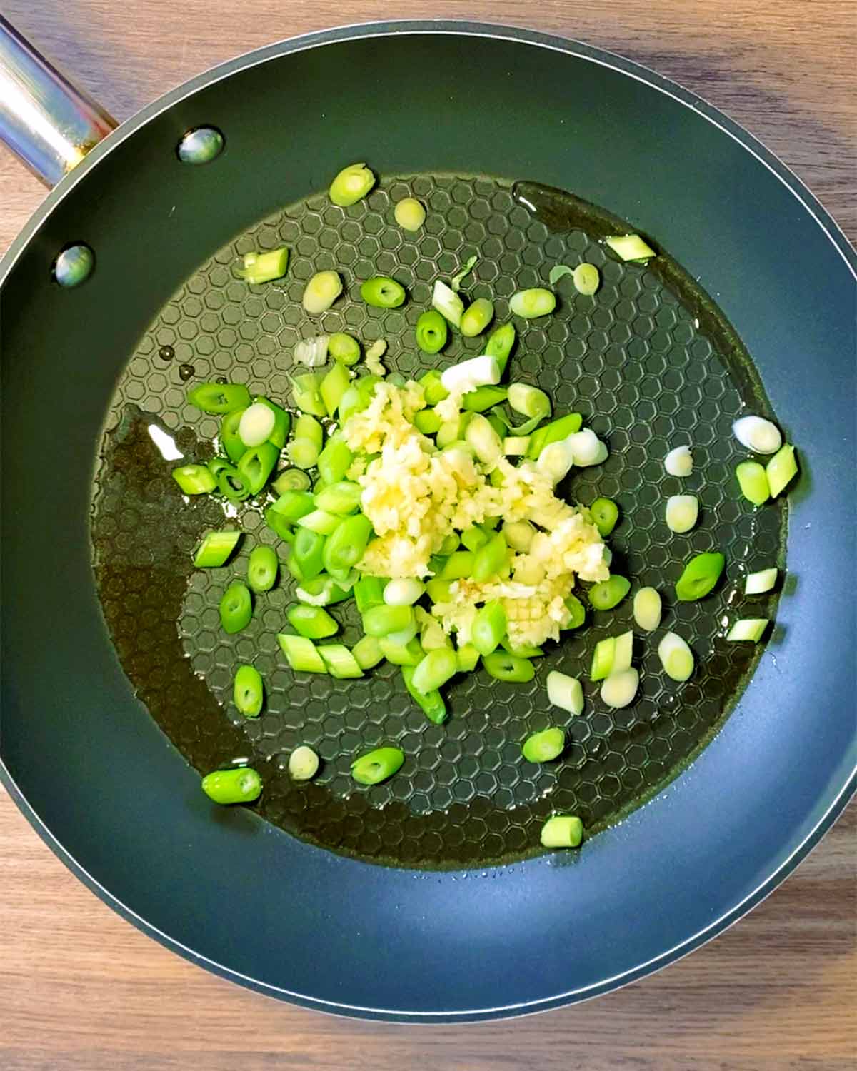 A frying pan with shopped spring onions and minced garlic cooking in it.