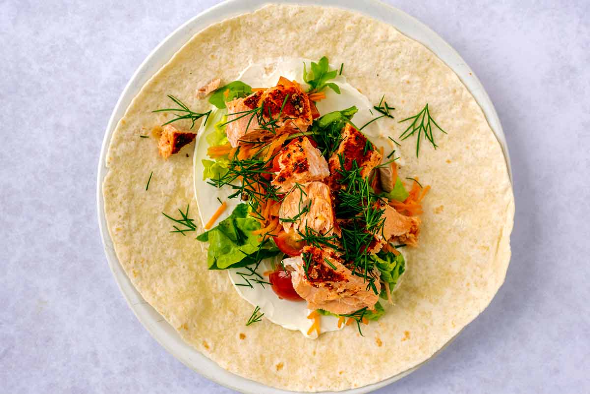 An open tortilla wrap with salad and flaked salmon on it.