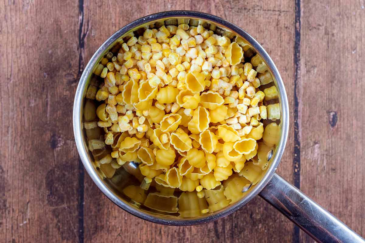 A saucepan containing uncooked conchiglie pasta and frozen sweetcorn.