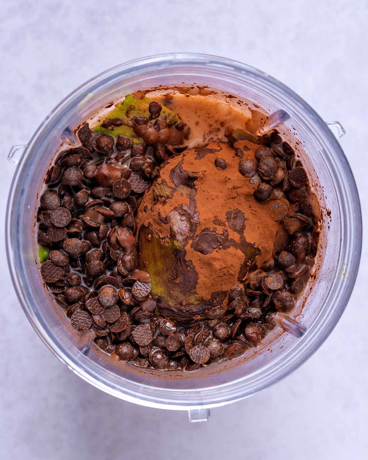 A blender jug containing avocado, cocoa, chocolate chips and maple syrup.