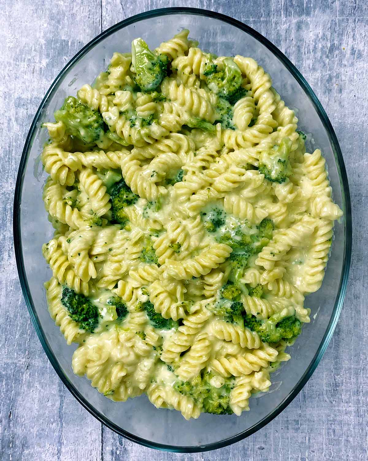 Cooked pasta and broccoli mixed with a cheese sauce all in an oval baking dish.