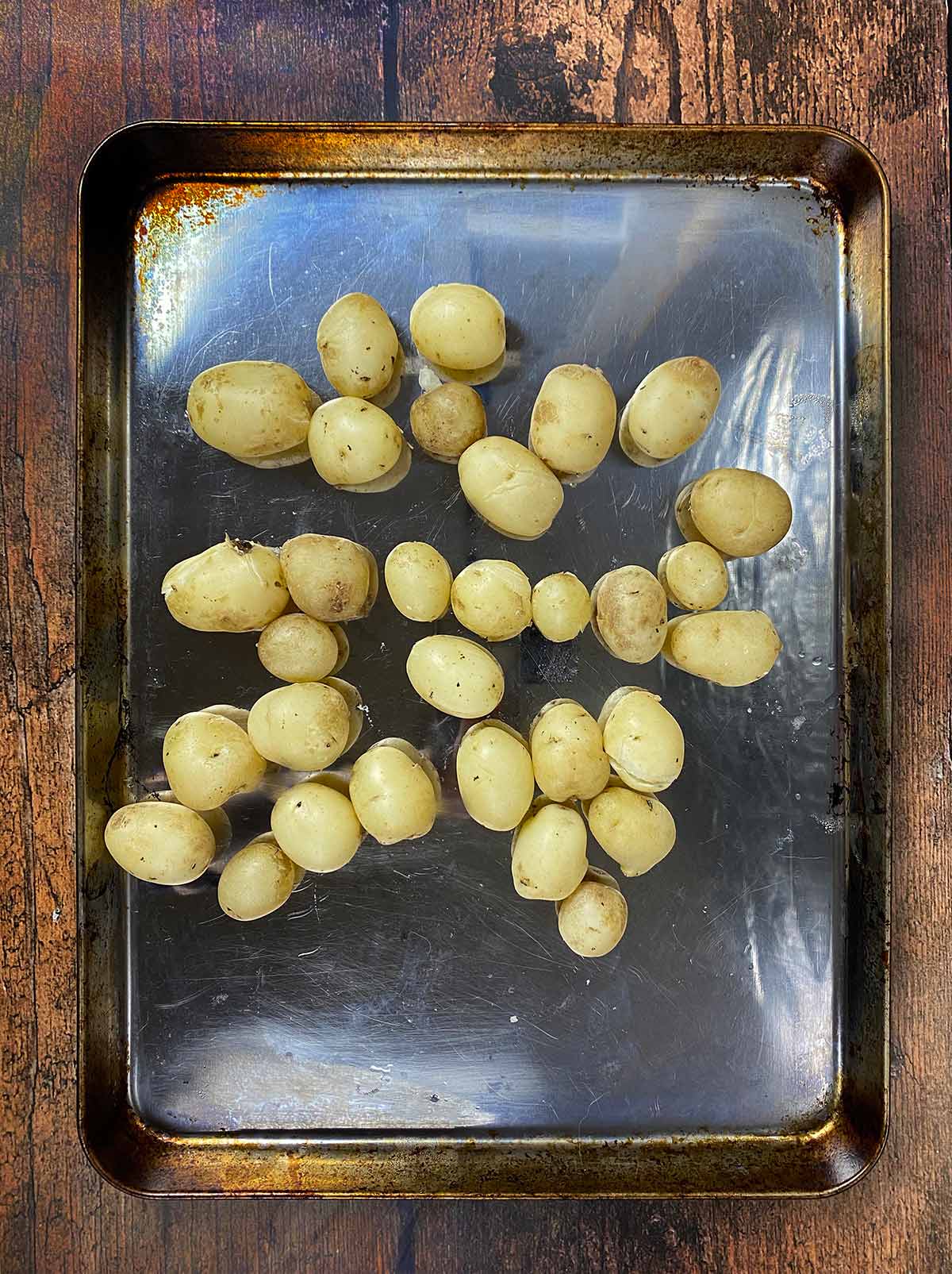 A baking tray with par-boiled new potatoes on it.