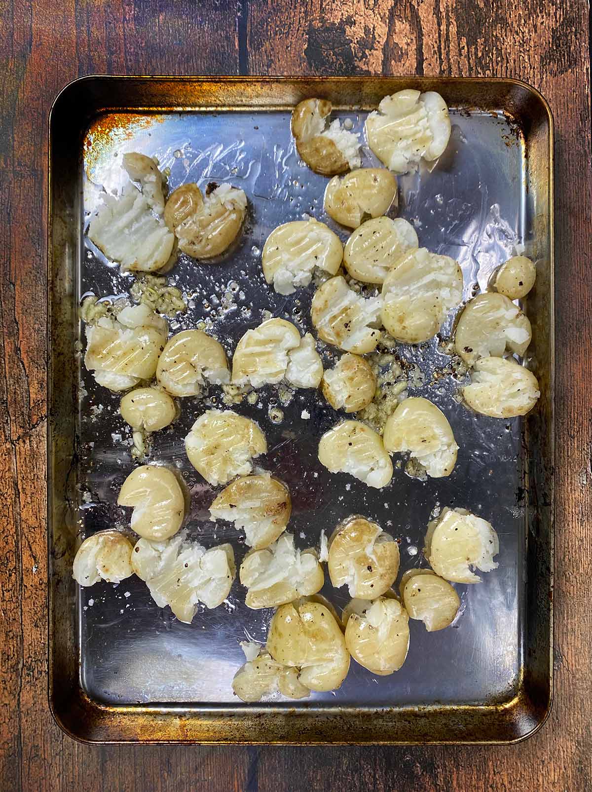 Part cooked potatoes on a baking tray that have been partly crushed.