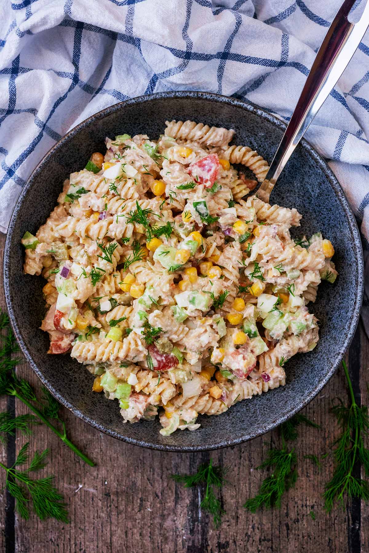 A large grey bowl of pasta salad with a spoon in it.