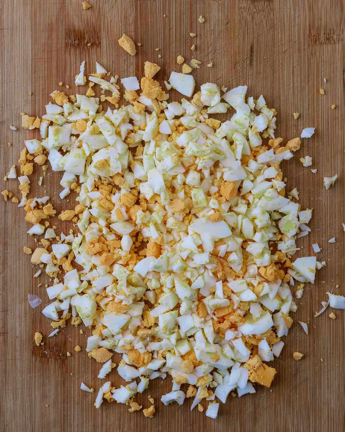 Hard boiled eggs chopped into small pieces on a wooden chopping board.