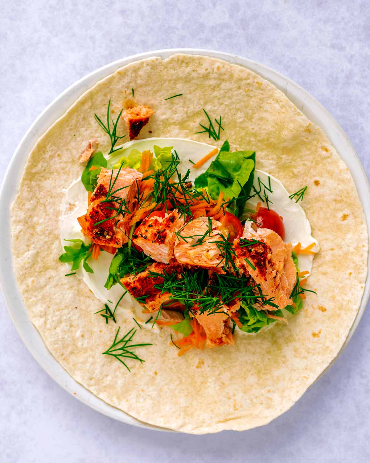 An open tortilla wrap with salad and flaked salmon on it.