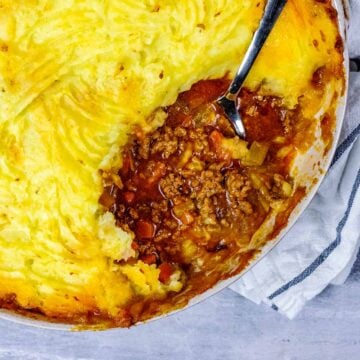 A large serving dish of shepherd's pie with a portion removed.