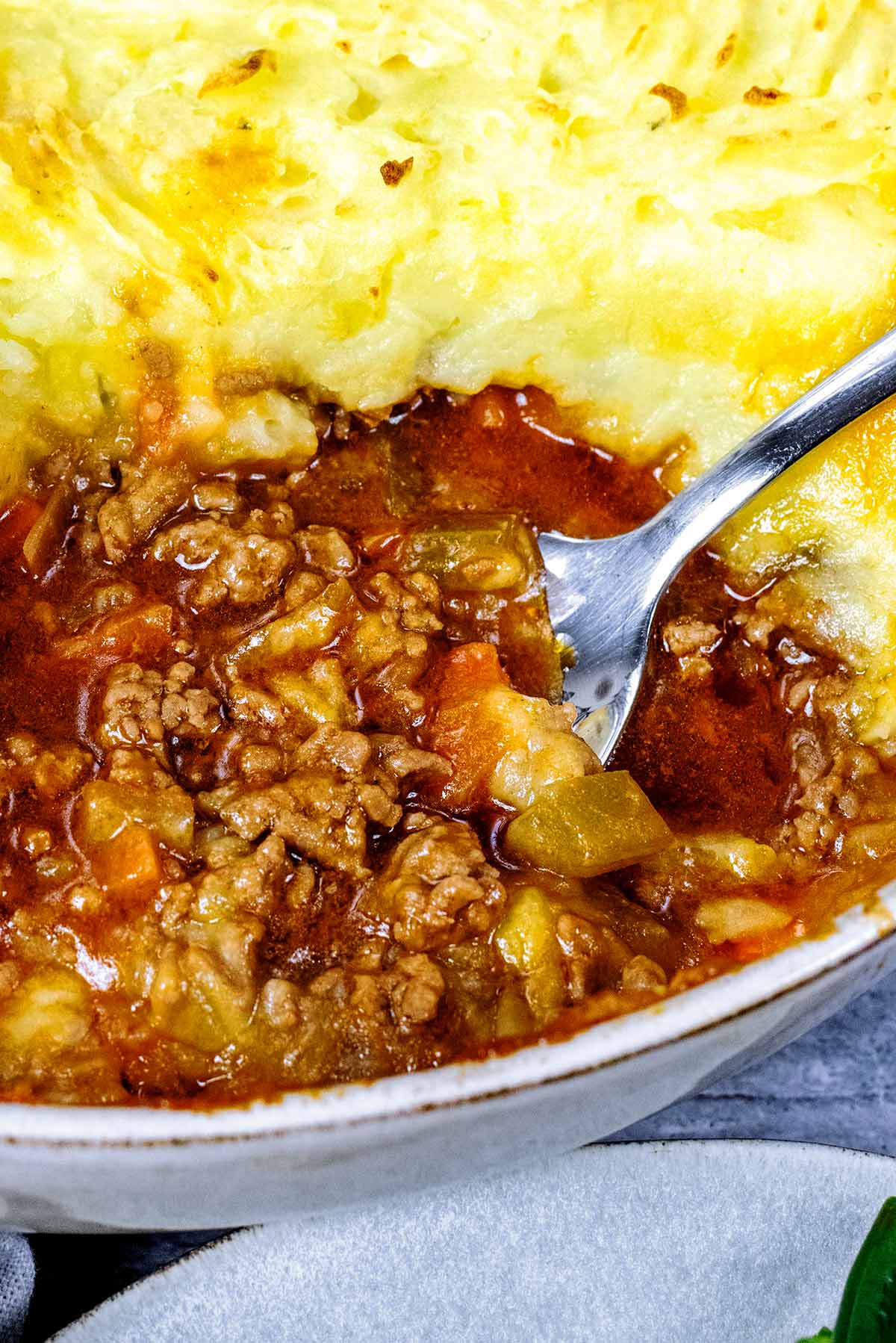 A spoon removing some mince from a large dish of shepherd's pie.