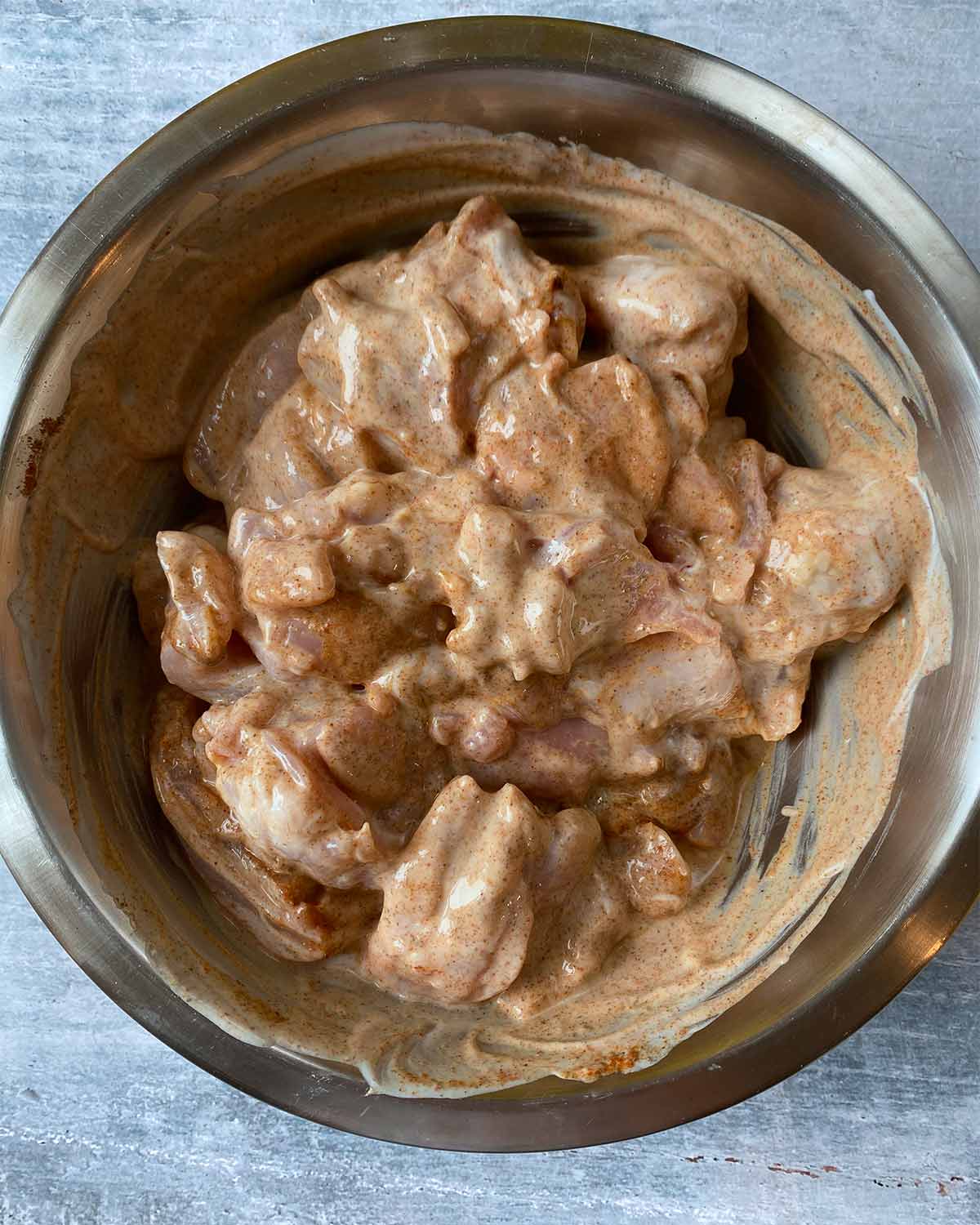 A bowl with chunks of chicken marinating in a brown yogurt sauce.