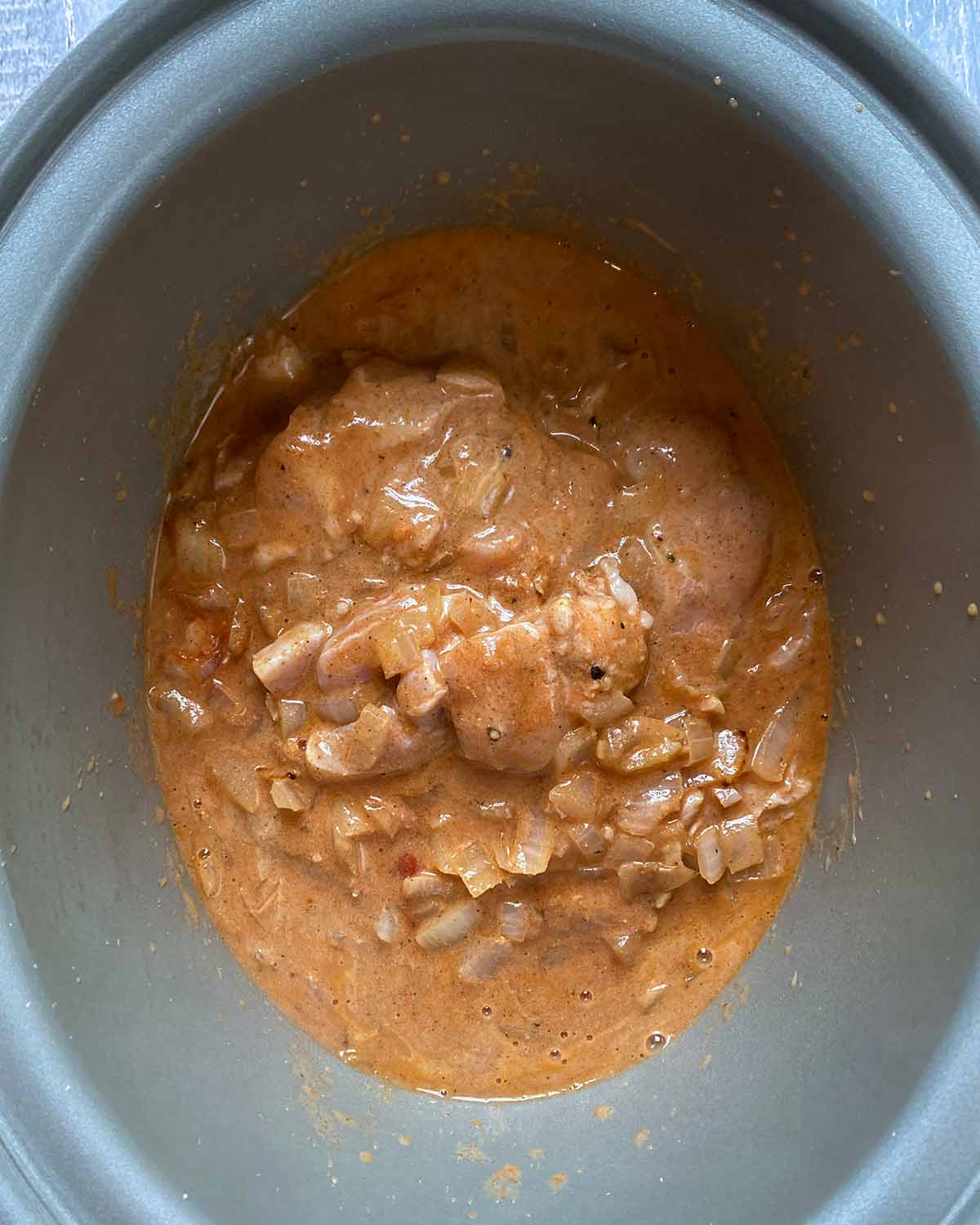 A slow cooker pot containing chicken chunks in a curry sauce.