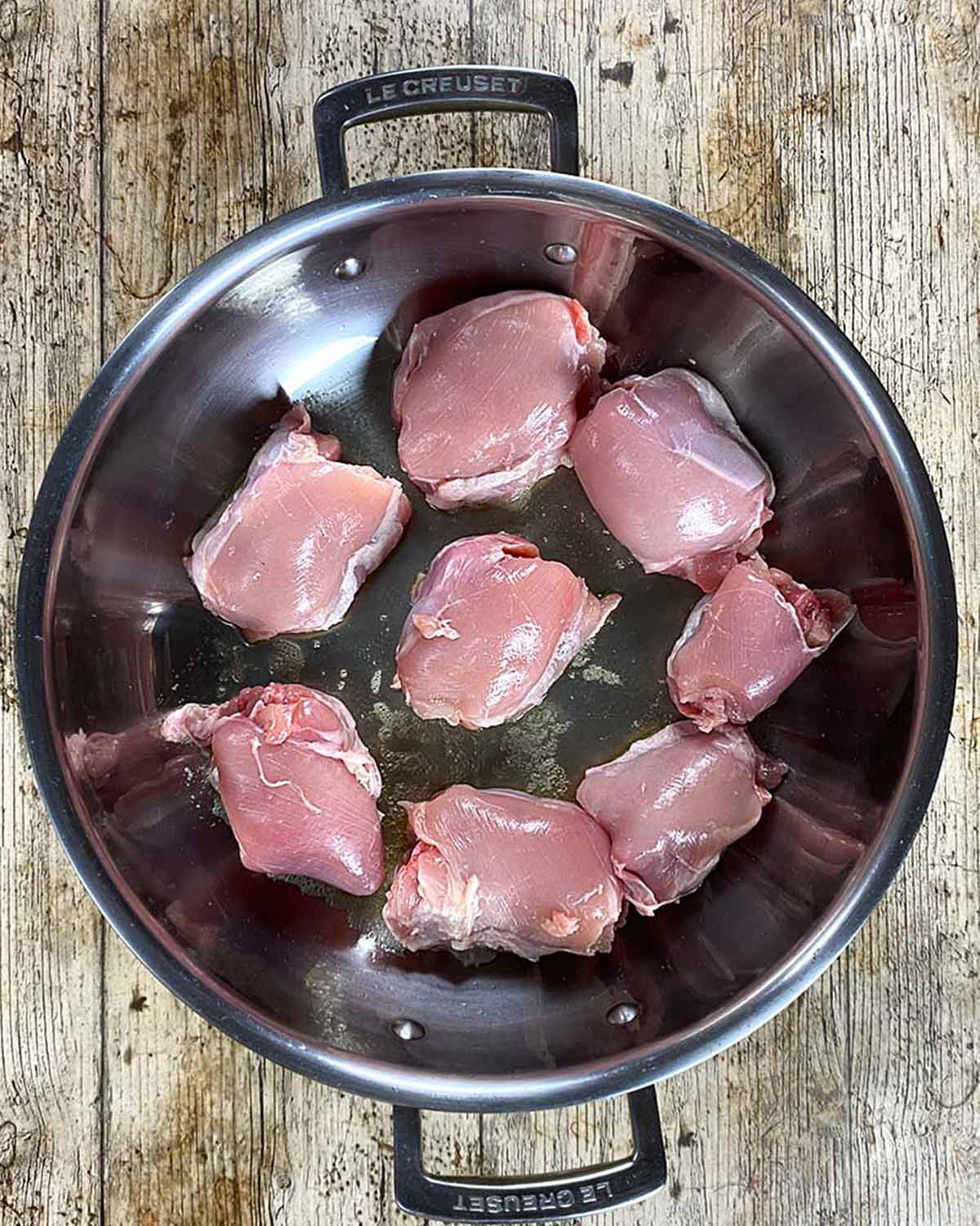 Eight chicken thighs browning in a large silver pan.