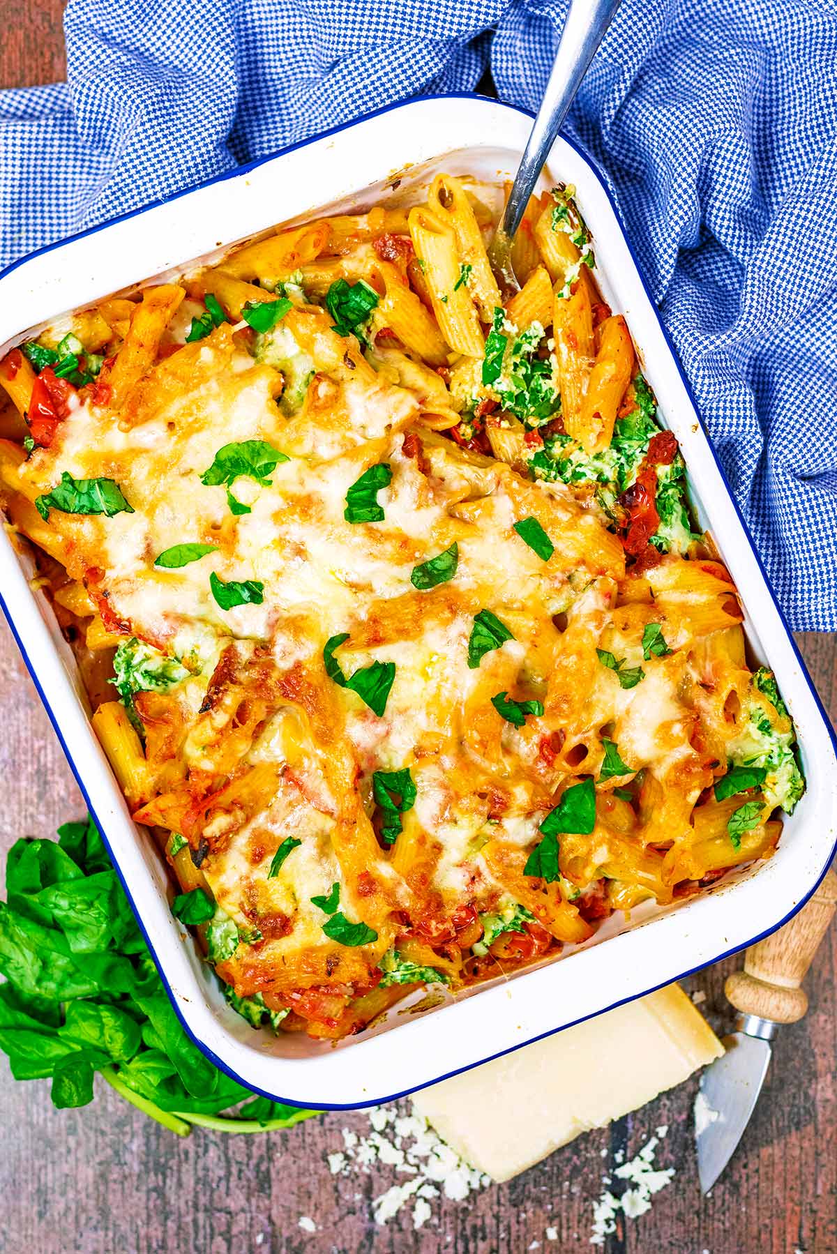 A large baking dish of pasta bake with a spoon in it.