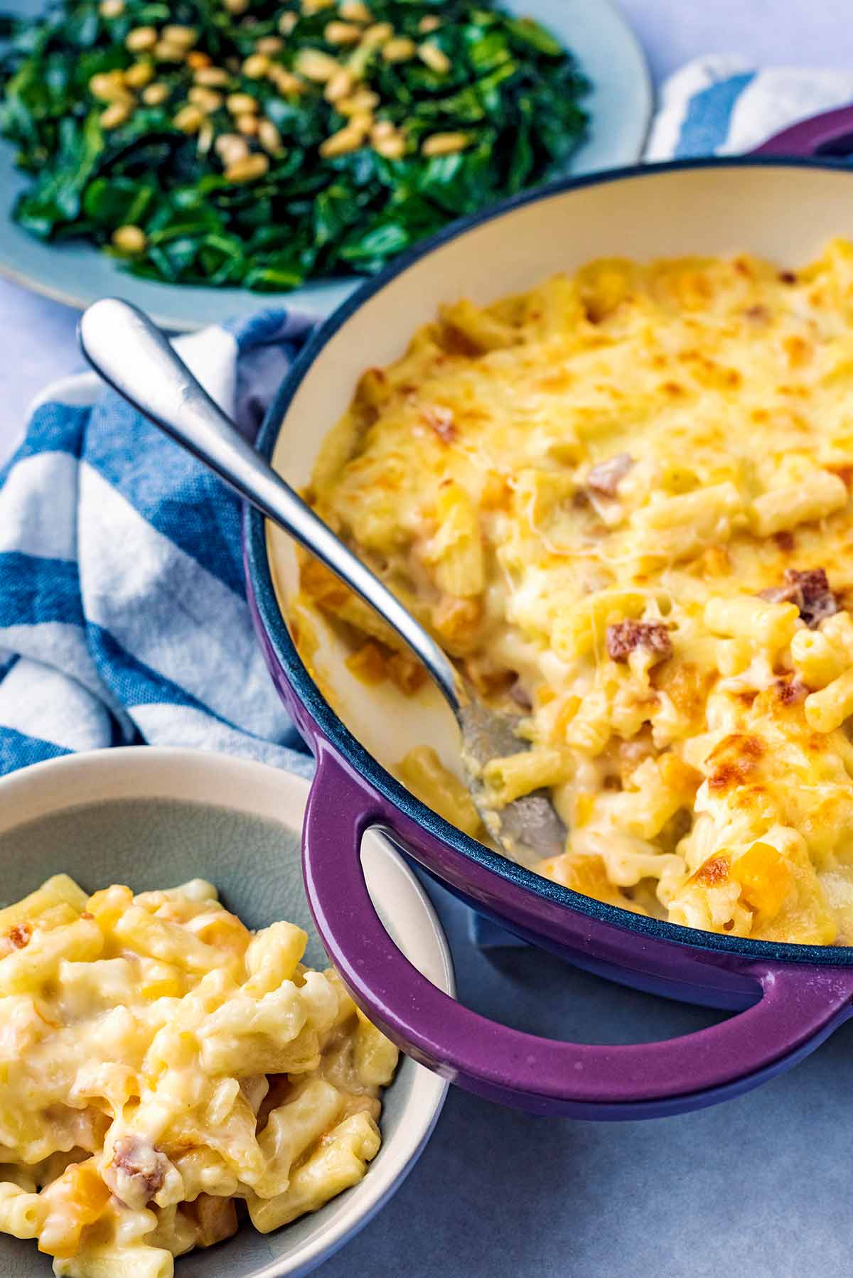 A baking dish full of macaroni cheese in front of a bowl of greens.