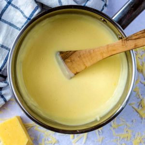 Easy Cheddar Cheese Sauce in a pan with a wooden spatula.