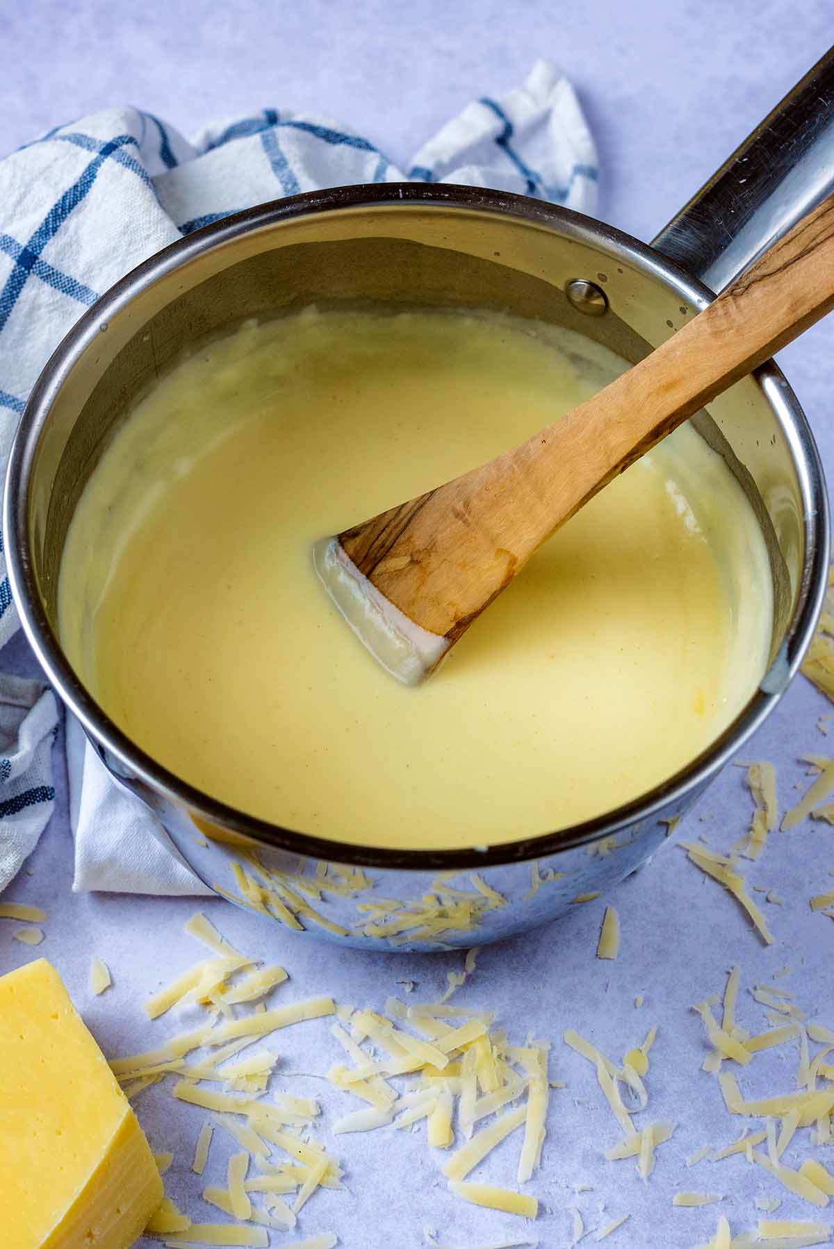 A wooden spatula in a pan of cheese sauce.