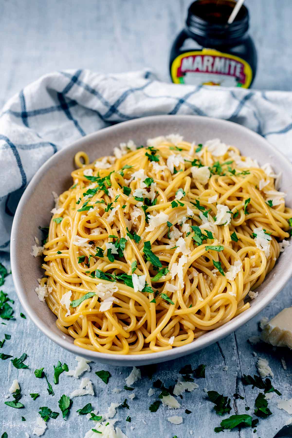 A bowl of spaghetti, cheese and parsley with a jar of Marmite in the background.