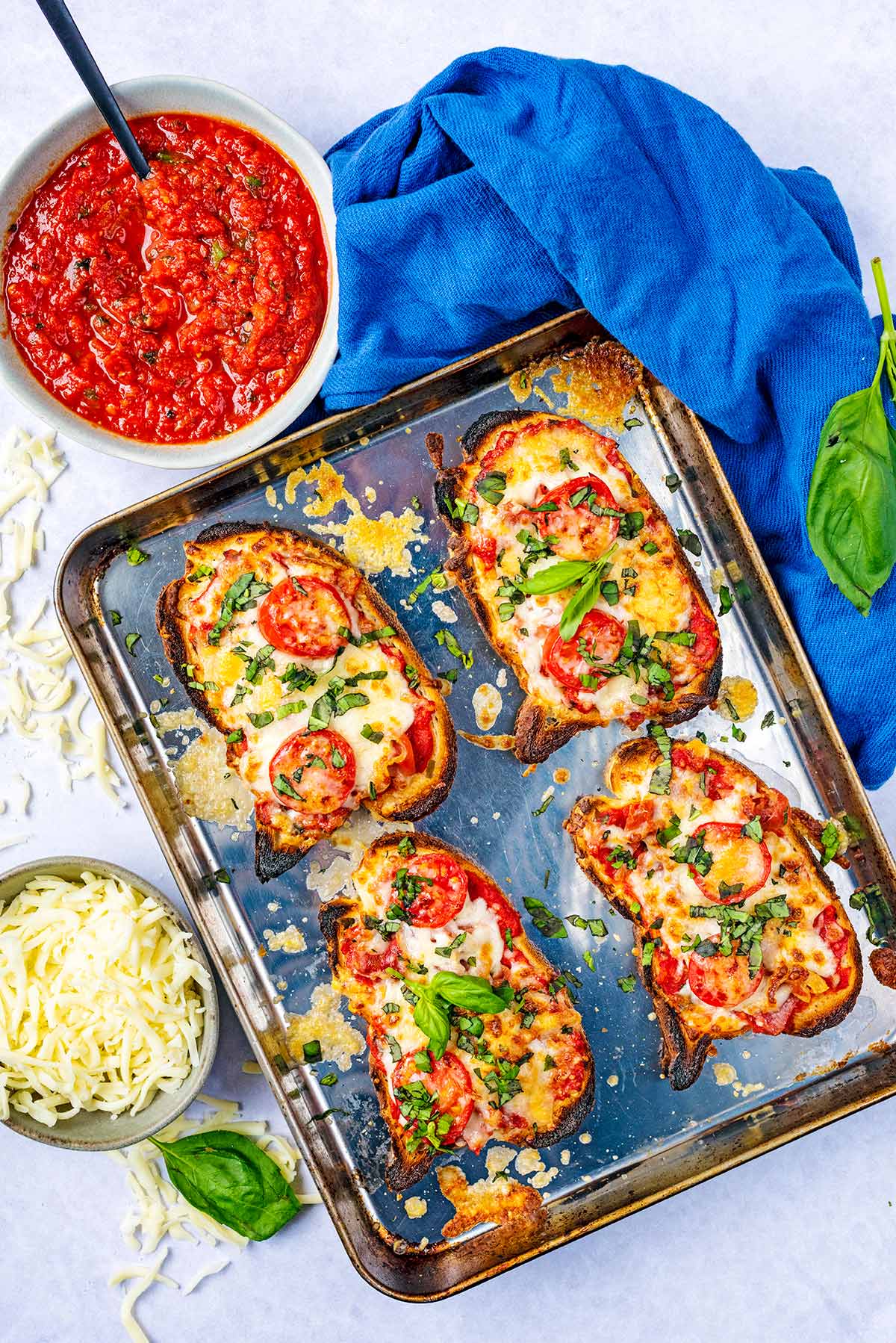 Four slices of pizza toast on a baking tray next to a bowl of pizza sauce.