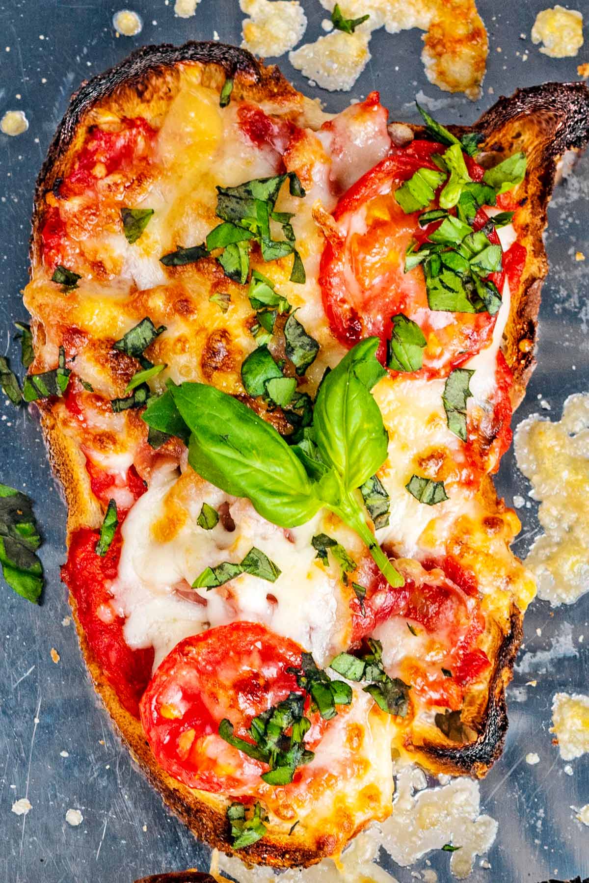 Melted cheese and tomatoes on toast with some basil leaves.