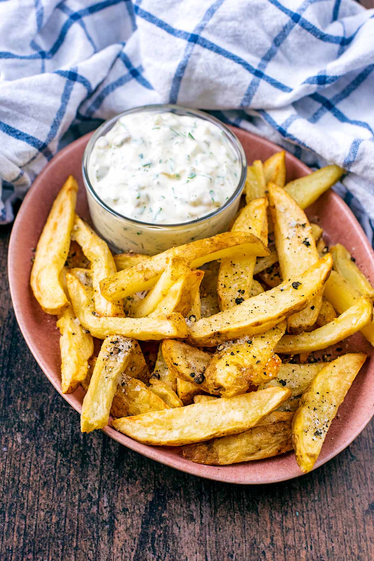 A plate of chips with a small pot of tartare sauce.