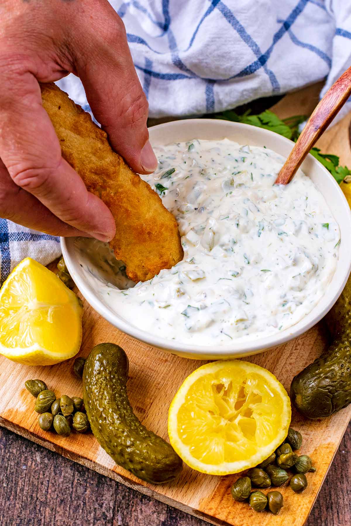 A hand dipping a fish finger into a bowl of tartare sauce.