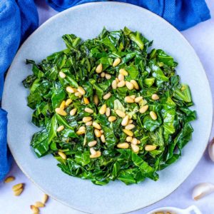 Garlic spring greens on a plate topped with pine nuts.