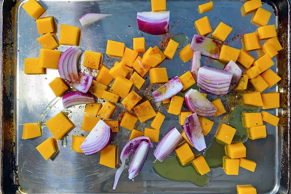 A baking tray with cubes of pumpkin and chopped red onion on it.