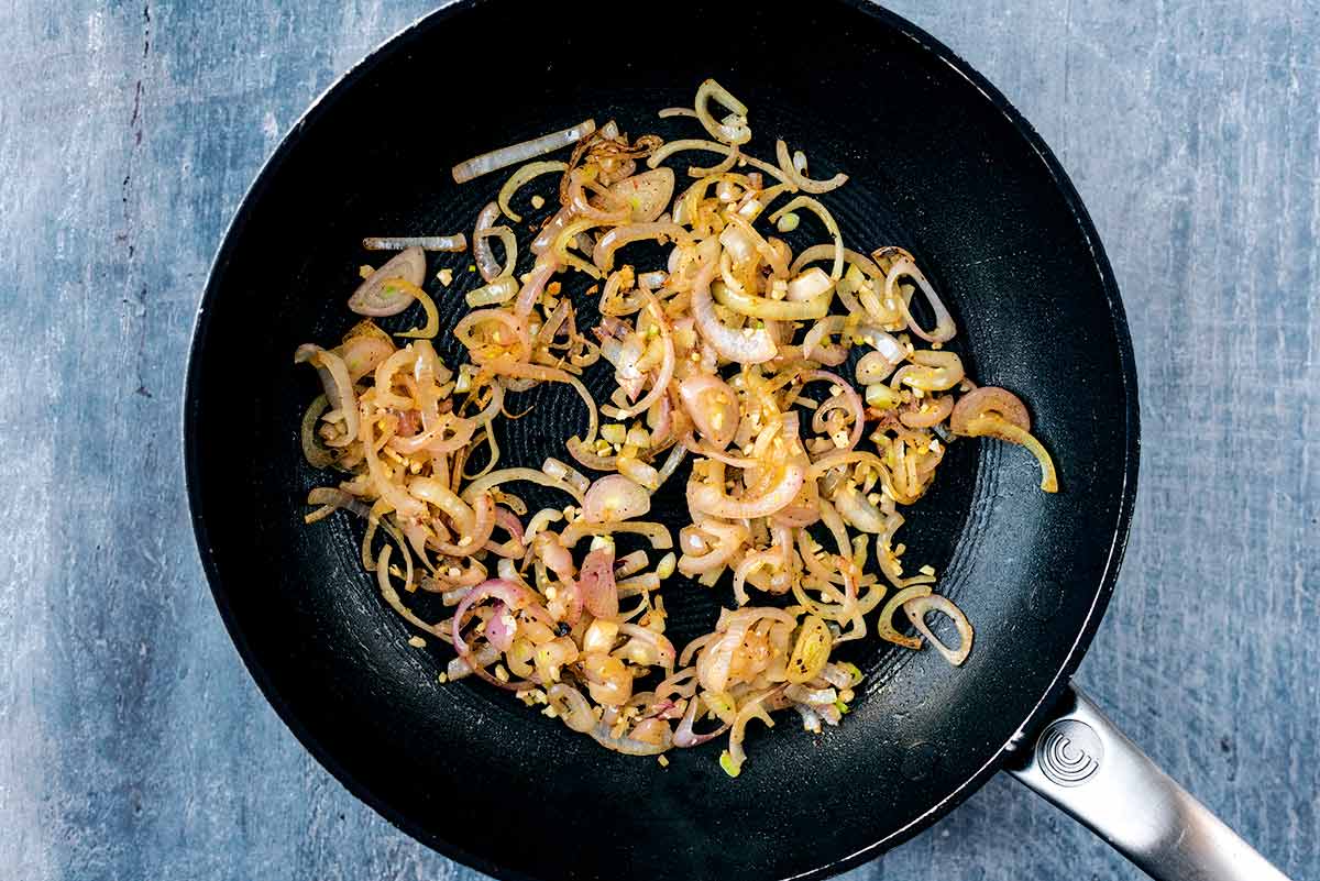 Sliced shallots and crushed garlic cooking in a frying pan.