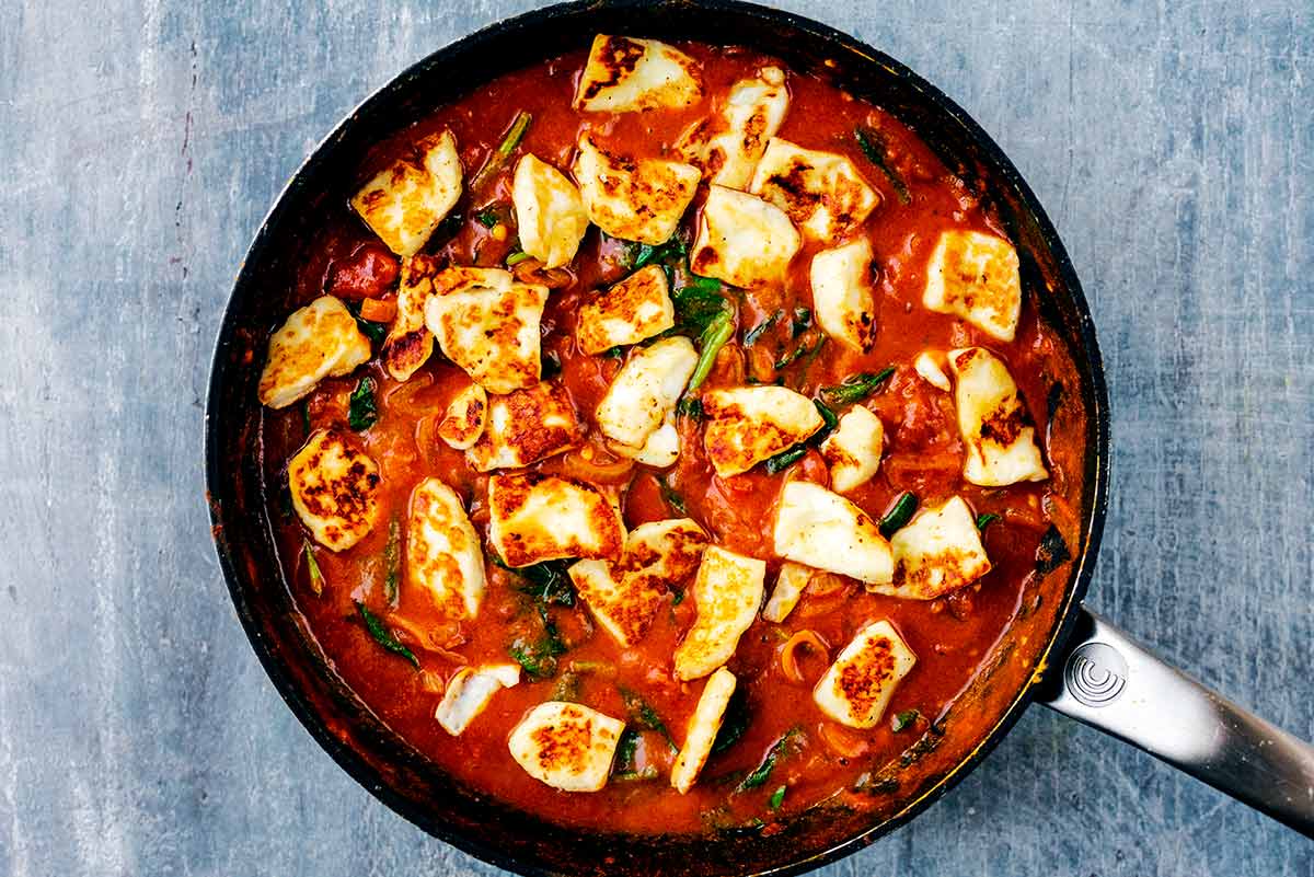Slices of halloumi cooking in a red curry sauce.
