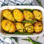 Eight hasselback potatoes in a baking dish with sprigs of rosemary.