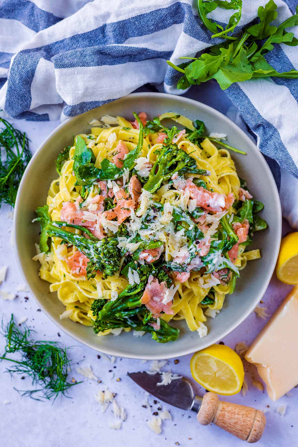 A bowl of salmon pasta next to a striped towel and some lemon halves.