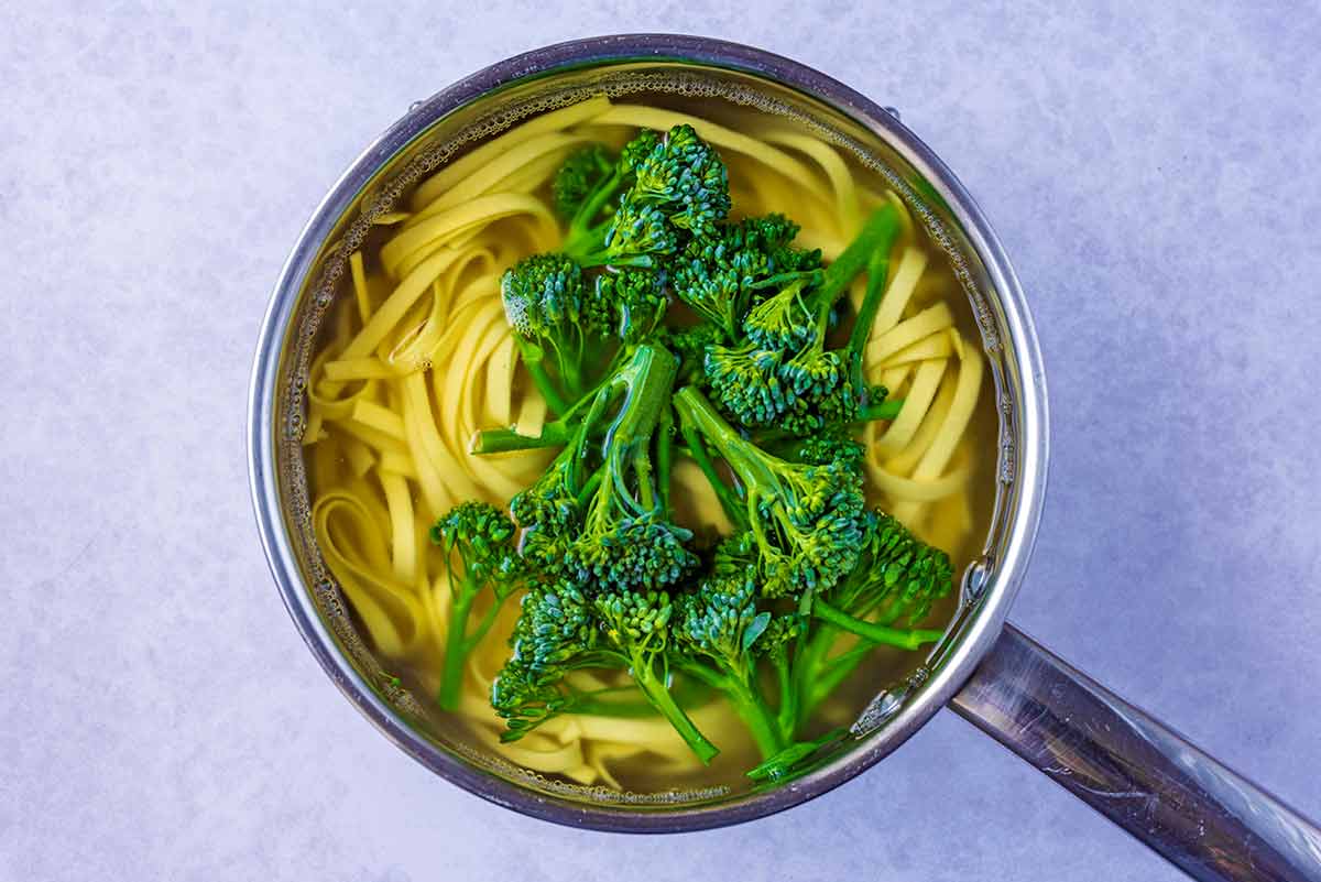 Tagliatelle and broccoli florets cooking in a pan.