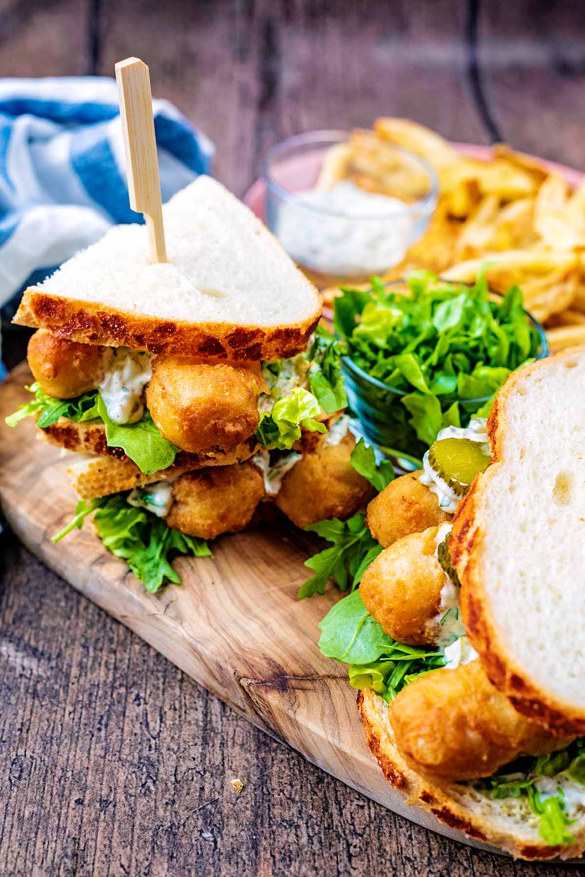 Two stacks of fish finger sandwiches on a wooden serving board.