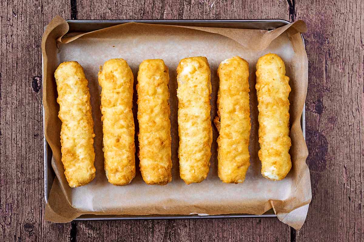 A bakng tray with six fish fingers on it.