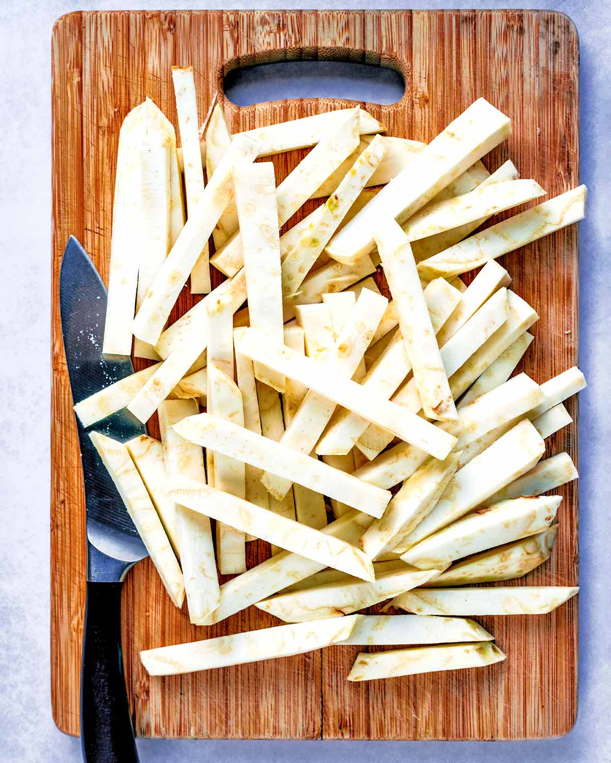 A chopping board and chef's knife with a pile of raw chips.