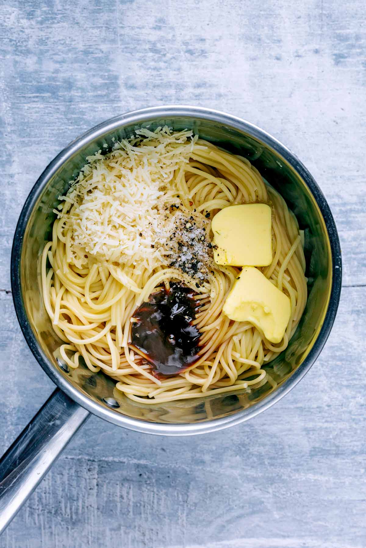 The pan of now cooked spaghetti with butter, cheese, Marmite and seasoning in it.