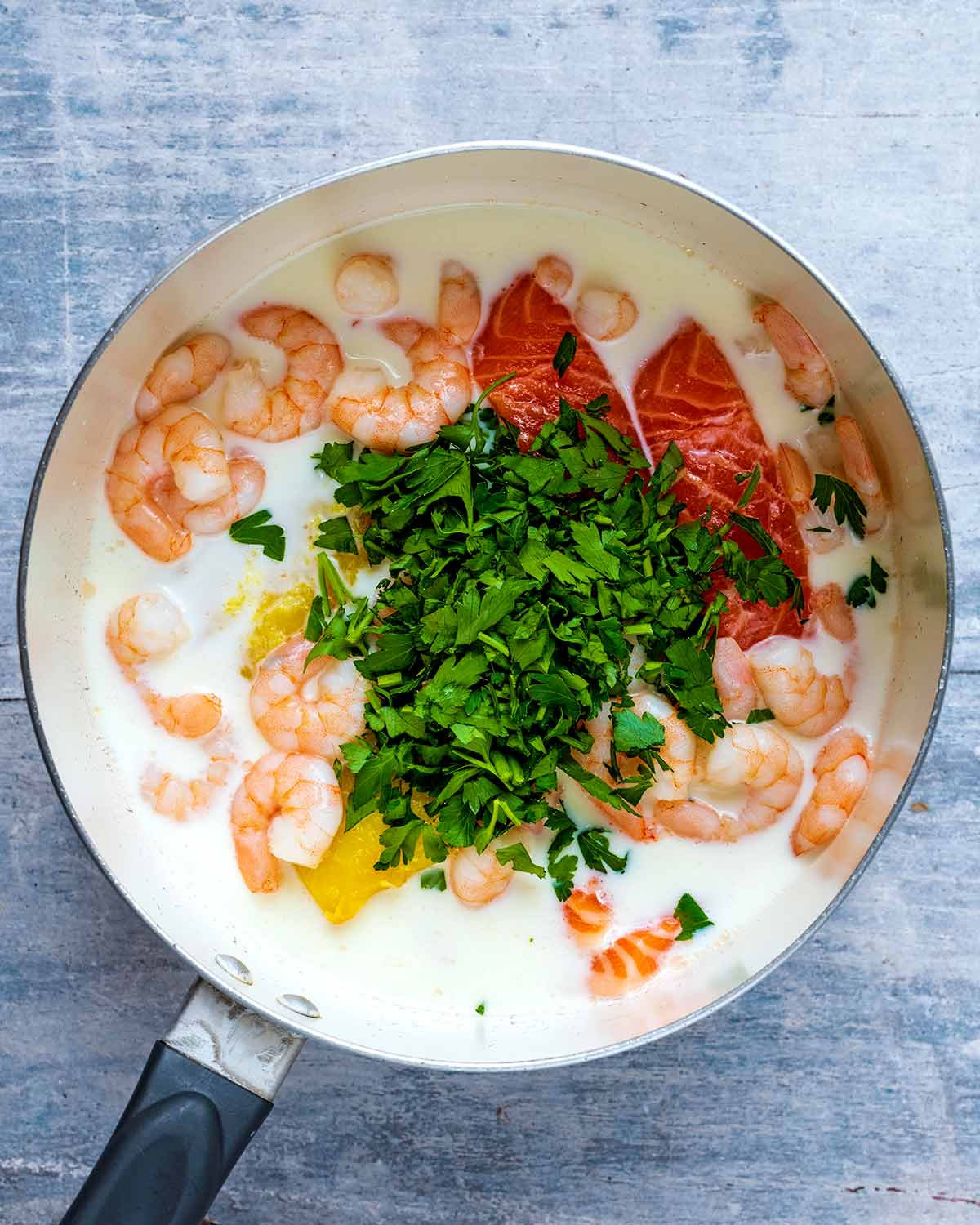 A saucepan full of milk, salmon, haddock, prawns and parsley.