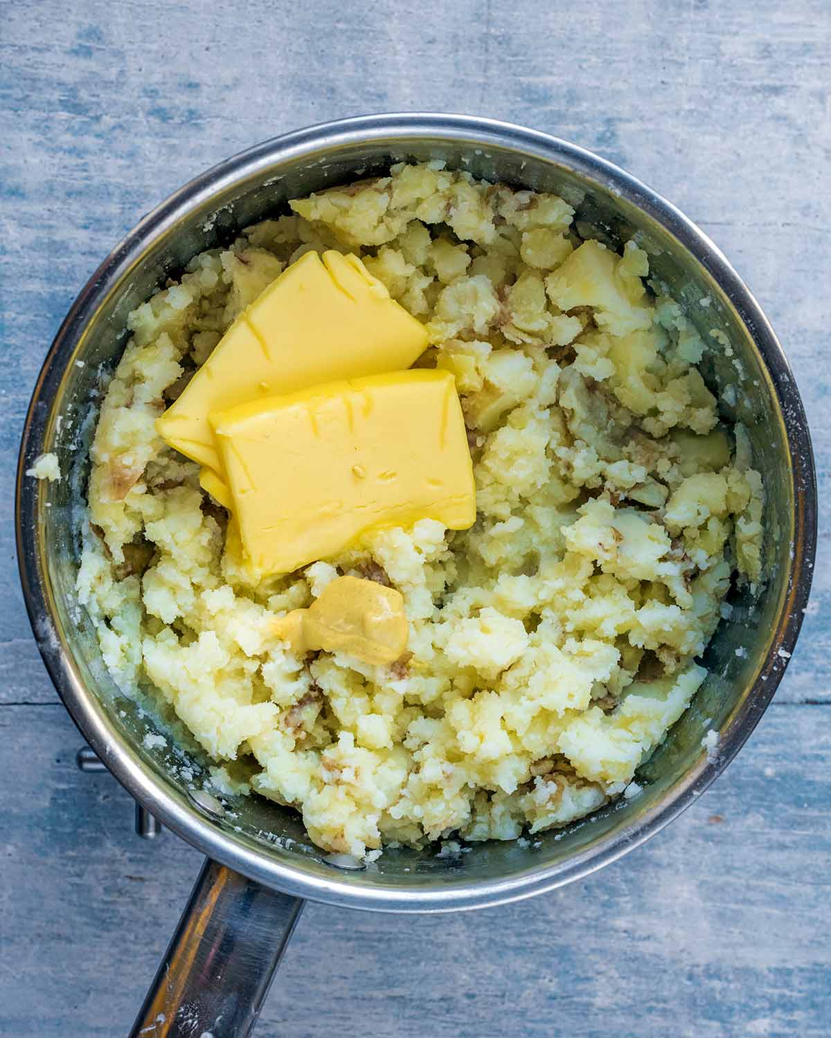 Mashed potatoes in a pan with pats of butter and a small dollop of mustard.