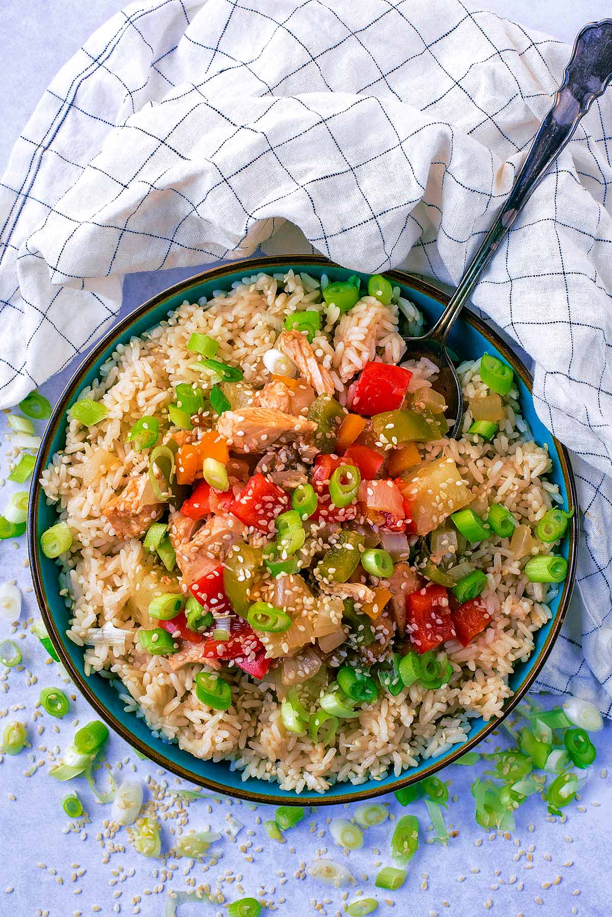 A large bowl of sweet and sour chicken and rice with a spoon in it.