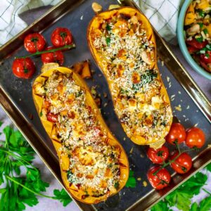 Stuffed butternut squash on a baking tray with cherry tomatoes.