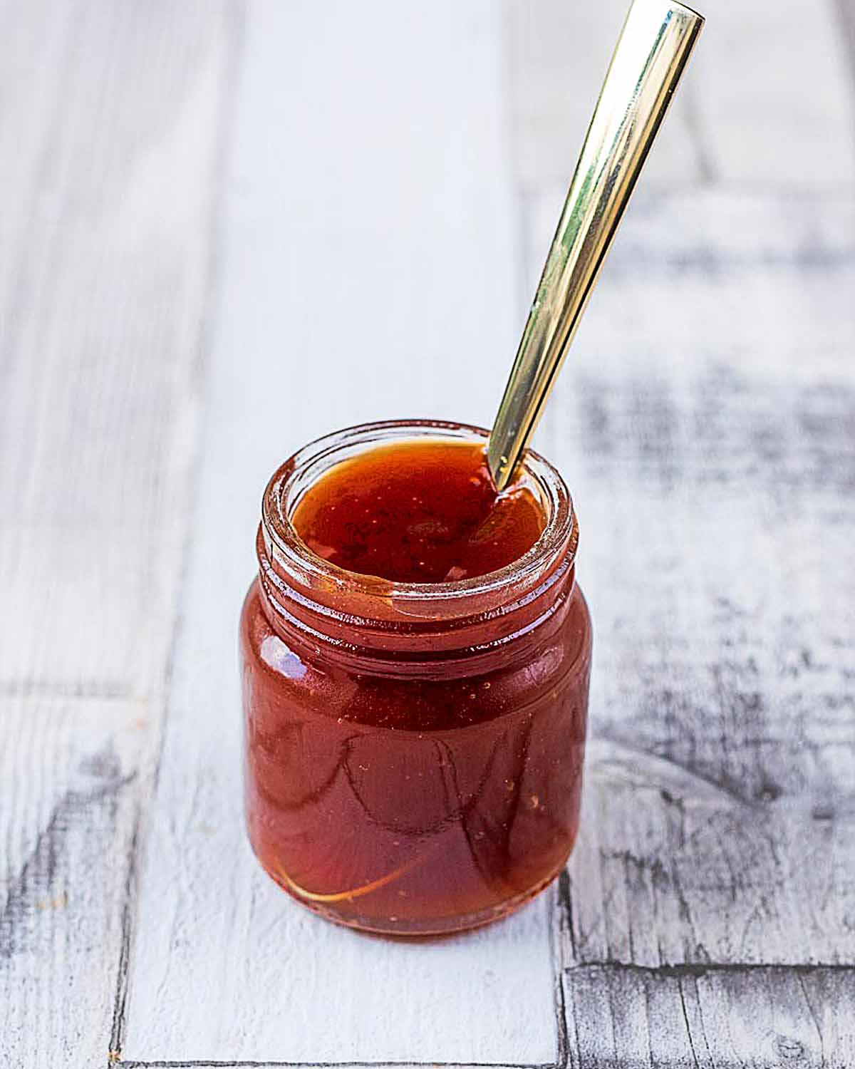 A small jar of sweet and sour sauce with a spoon sticking out of it