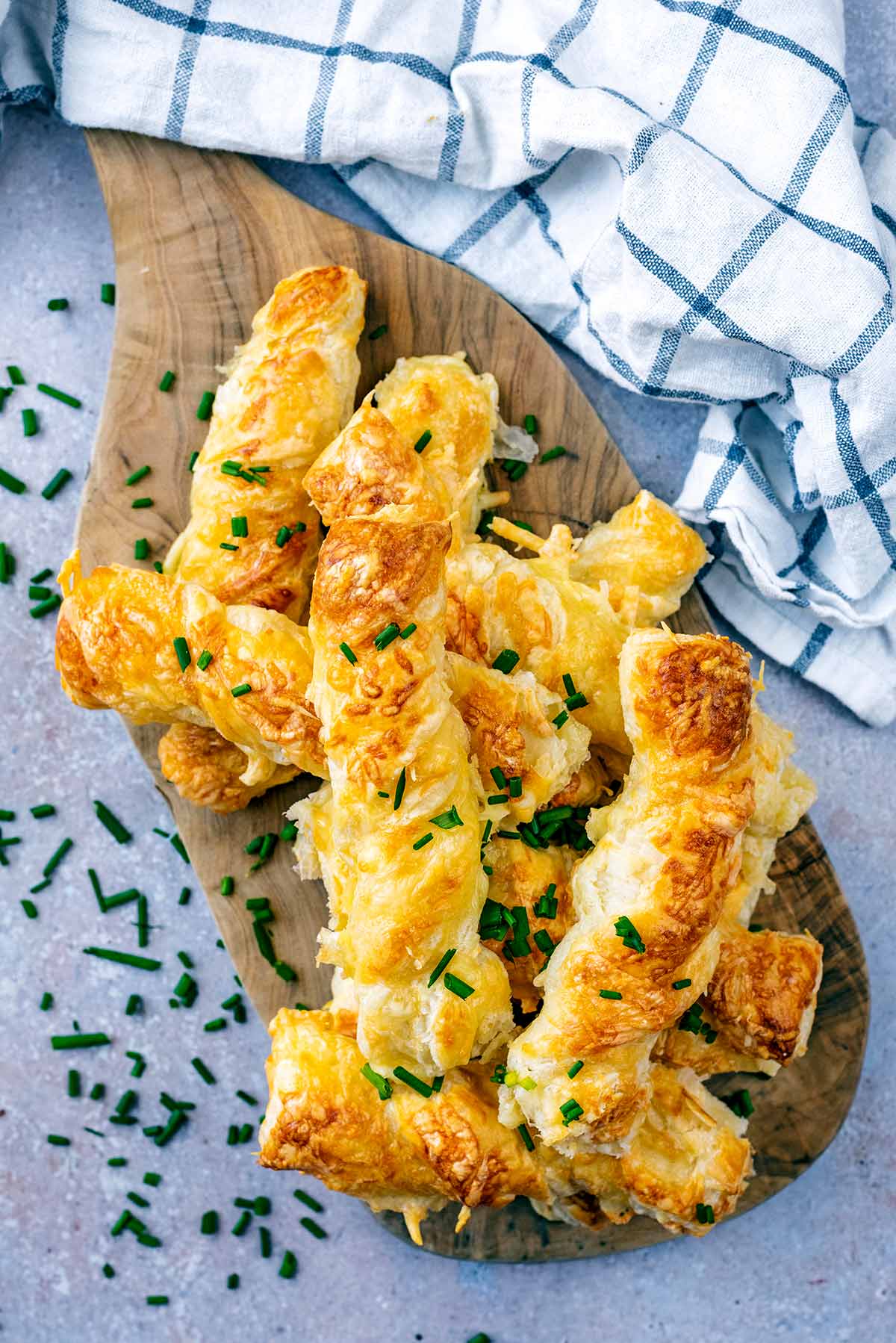 A pile of cheese straws on a wooden serving board.