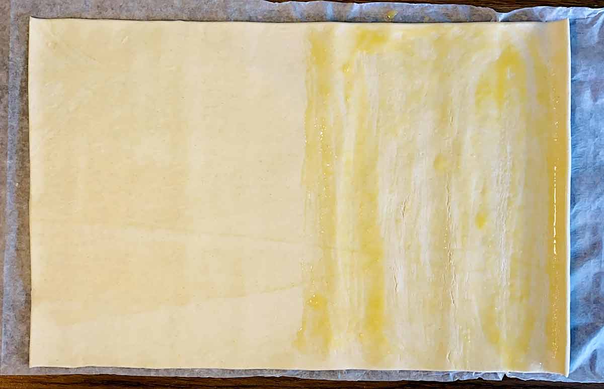A sheet of puff pastry with half of it covered in egg wash.