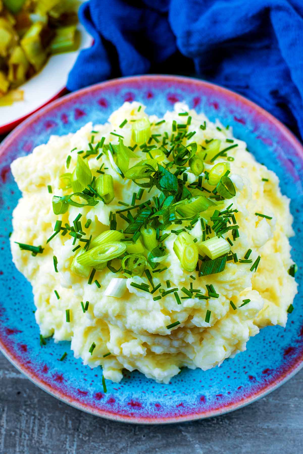Mashed potatoes on a blue plate topped with sliced spring onions.