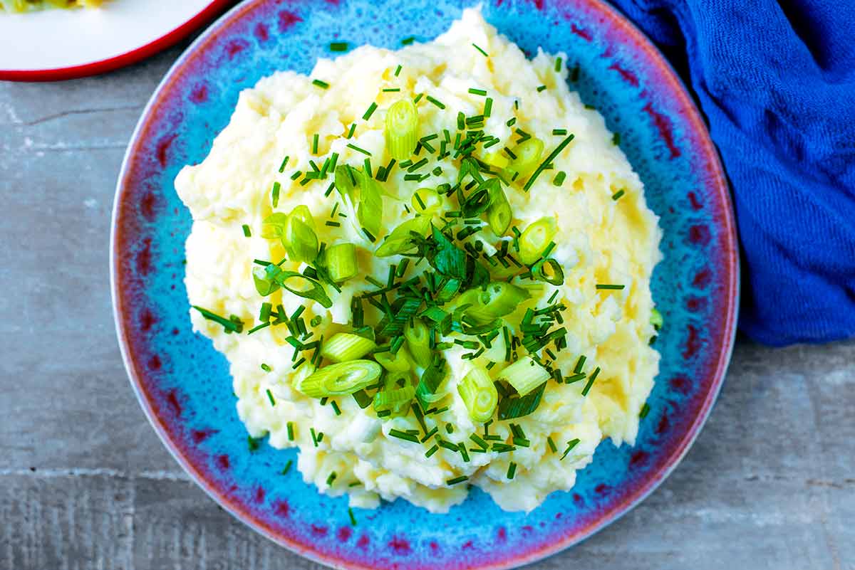 A plate of mashed potato with herbs and green onions.