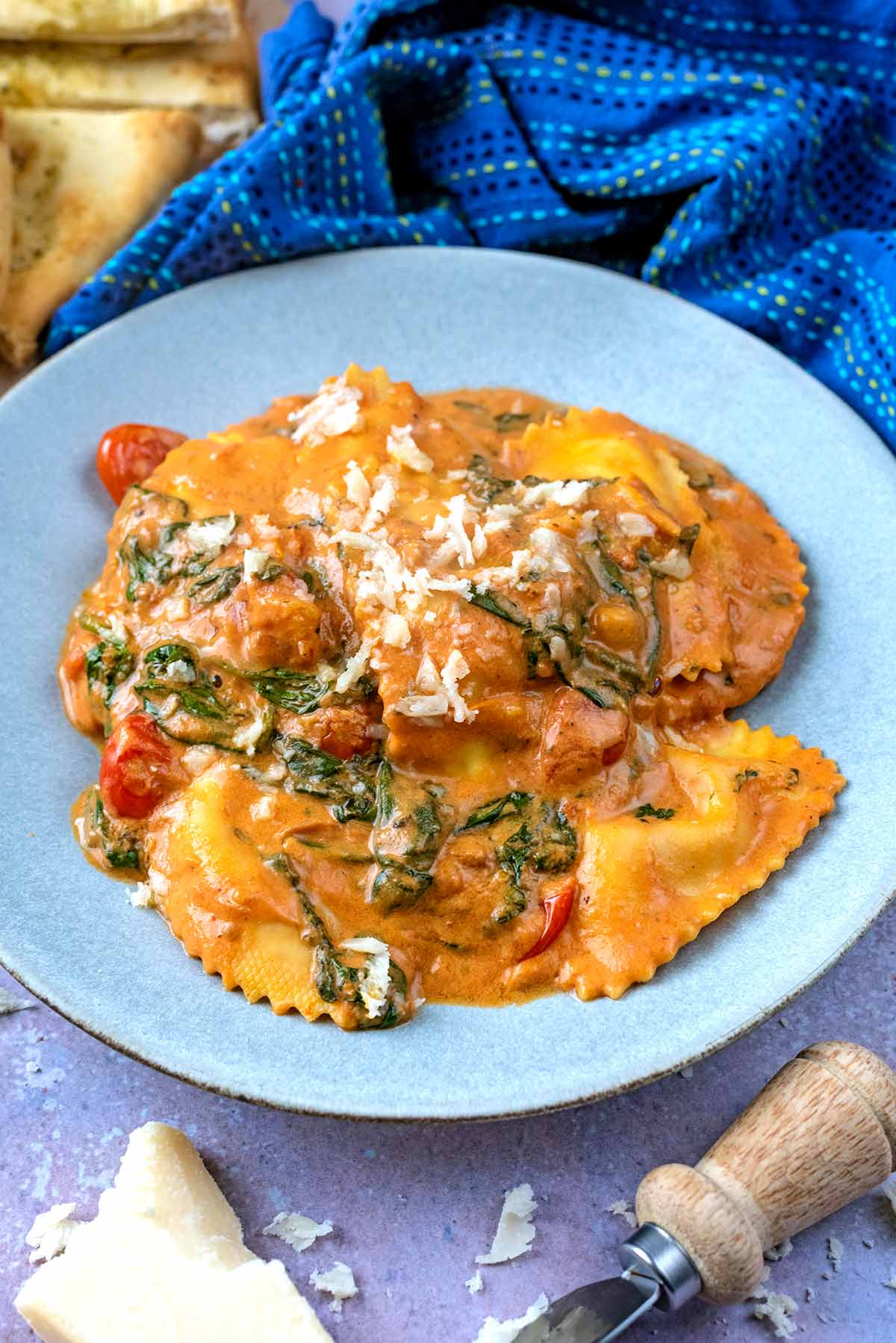 A plate of ravioli in sauce topped with Parmesan shavings.