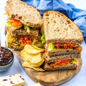 Epic cheese sandwich on a wooden board with potato crisps.