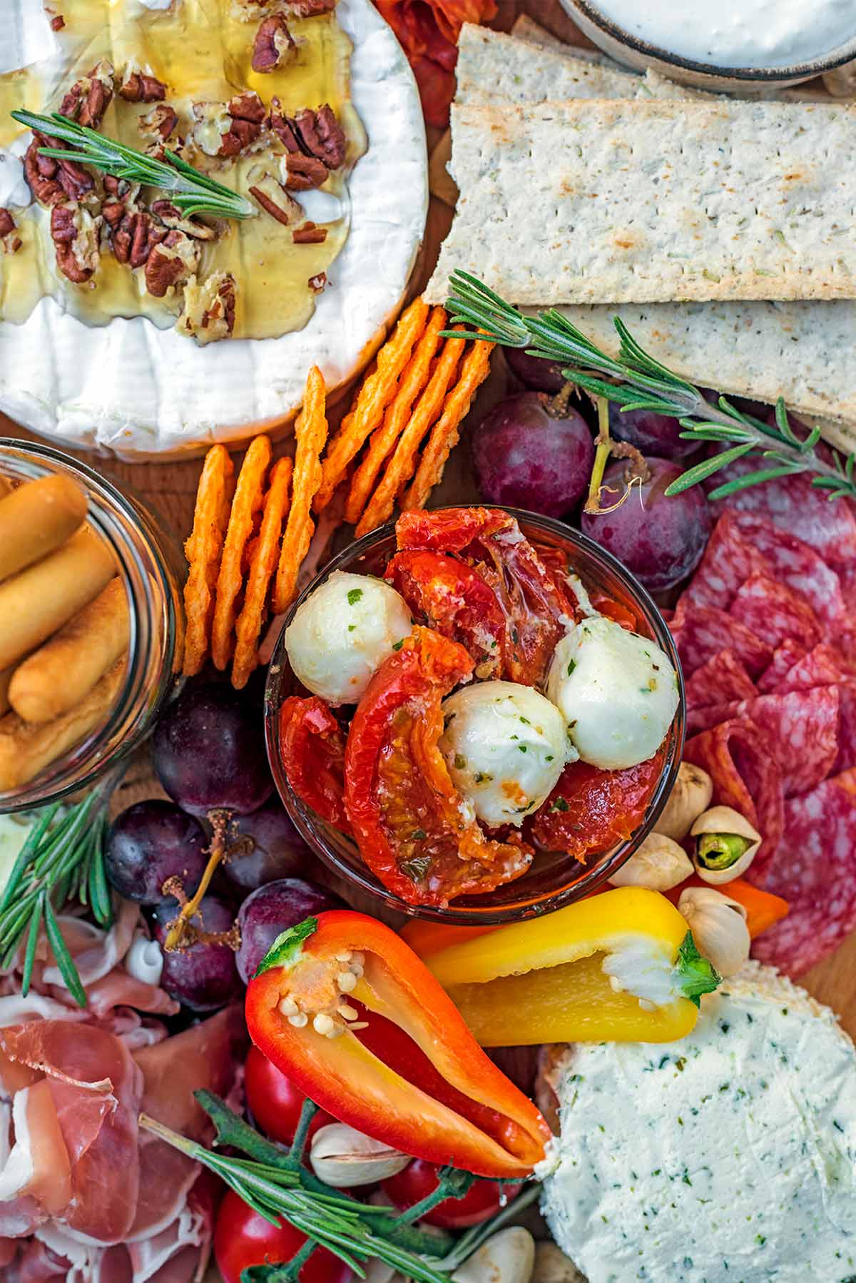 Sun-dried tomatoes, cheese, cured meats, grapes and crackers al together on a board.