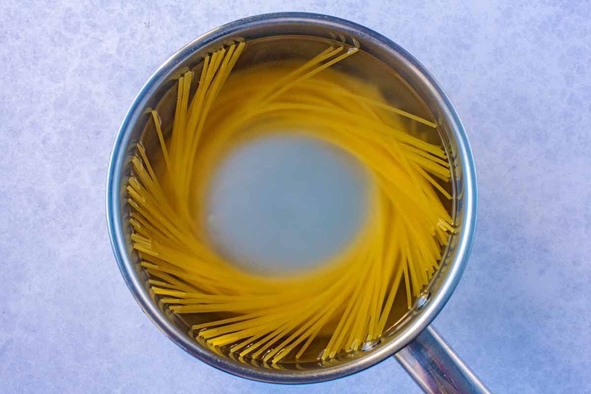 A saucepan containing spaghetti cooking in water.
