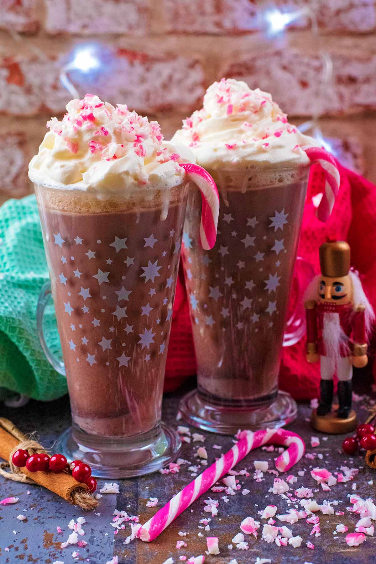 Two tall glasses of hot chocolate topped with cream and candy canes.