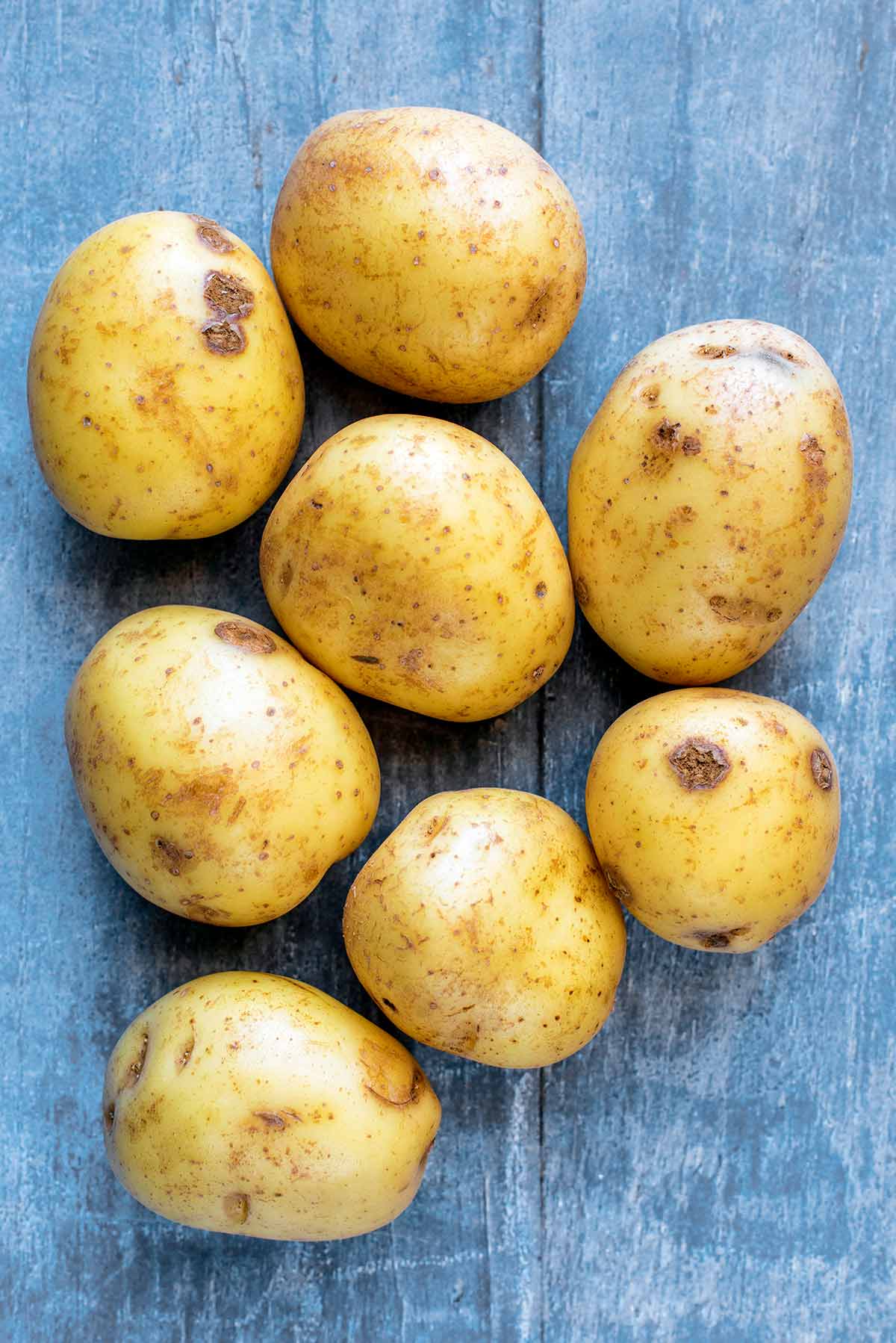 Eight potatoes on a wooden surface.